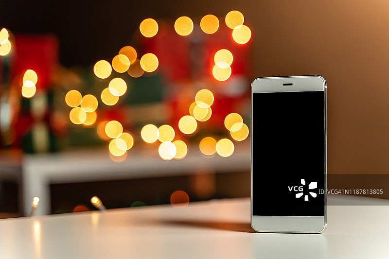 白色桌子上的智能手机，散焦圣诞灯和圣诞礼物的背景，散焦图片素材