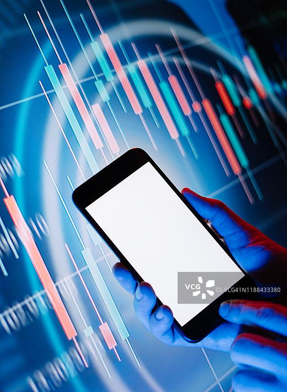 男性双手拿着智能手机，前面是一个显示金融信息的数字显示屏。空白的空屏幕。模拟了图片素材