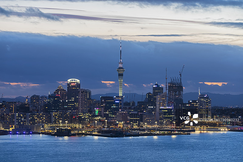 在新西兰大洋洲的黄昏，在多云的天空下，照亮了海上的现代建筑图片素材