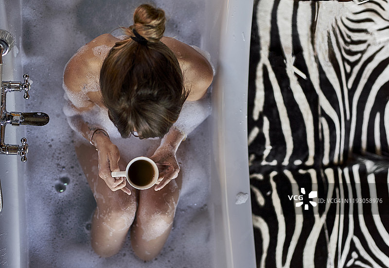 一个女人正在浴缸里放松地洗着澡，喝着咖啡图片素材
