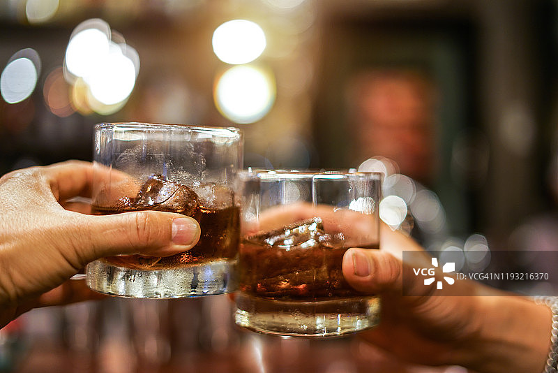 两名男子在酒吧柜台边碰杯喝着酒精饮料图片素材