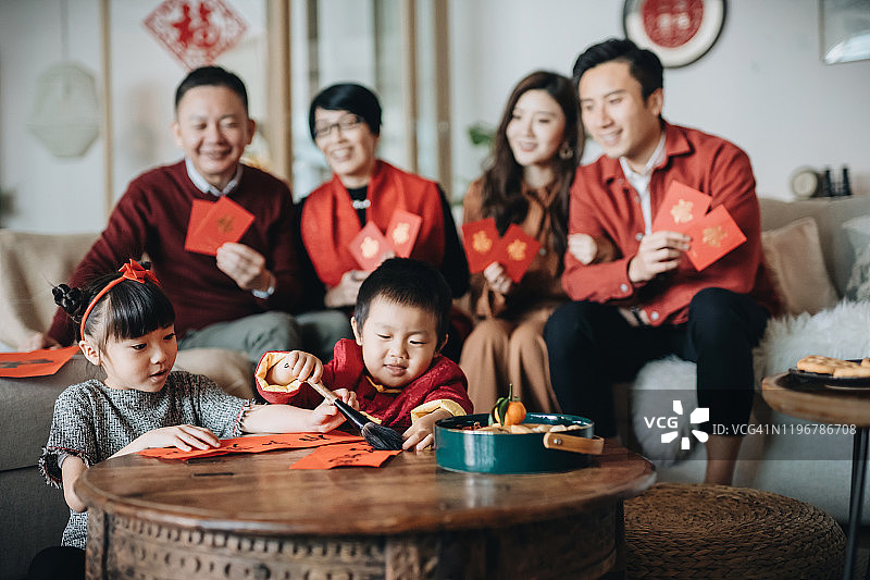 三代快乐的亚洲家庭庆祝农历新年，手里拿着“红包”，小朋友在前面练习书法，写“中国新年吉祥信息”图片素材