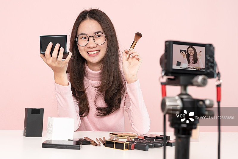 亚洲女性专业美容视频博主或博主通过相机在社交媒体上直播化妆教程的病毒视频剪辑。商业在线影响者对社交媒体的概念。在线销售。网上购物图片素材