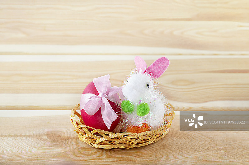 小玩具兔子在篮子与装饰复活节粉红色蝴蝶结在木制的背景图片素材