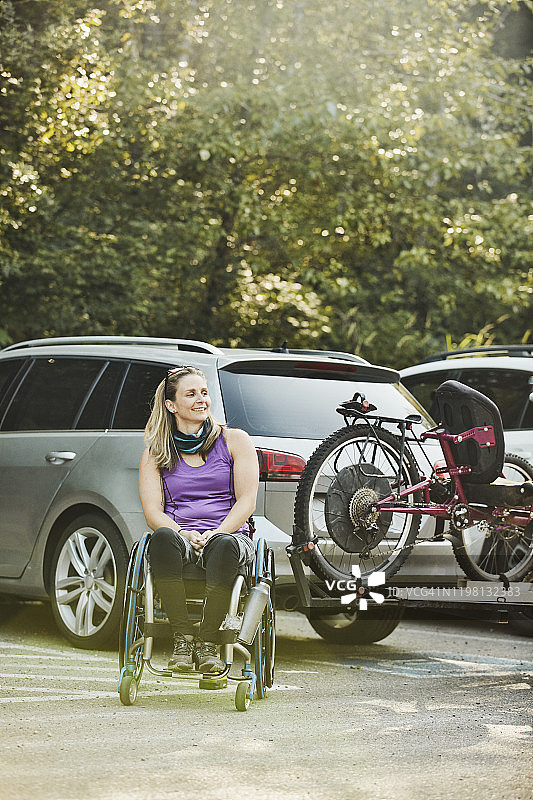 微笑的女性轮椅运动员的肖像在后面的汽车装载适应性山地车之前骑图片素材
