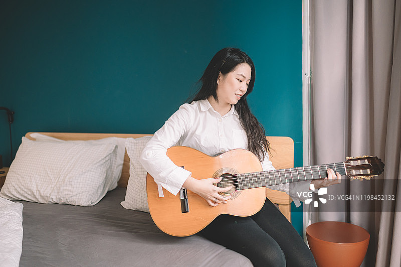 1名亚洲华人女性在卧室沙发上弹吉他图片素材