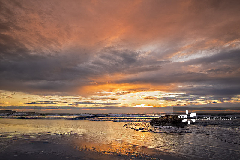 新西兰，汤加普鲁图，橙色黄昏，多云的天空笼罩在沙滩上图片素材