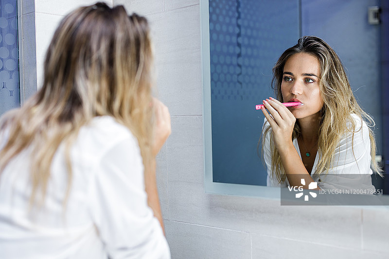 镜子里的映像是一个年轻漂亮的女人在浴室里刷牙。图片素材