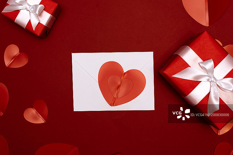 一个礼物在牛皮纸盒与一个红色的蝴蝶结在红色的背景与心。给你的爱人一个惊喜。情人节的概念有婚礼、生日、新年、圣诞节等节日图片素材
