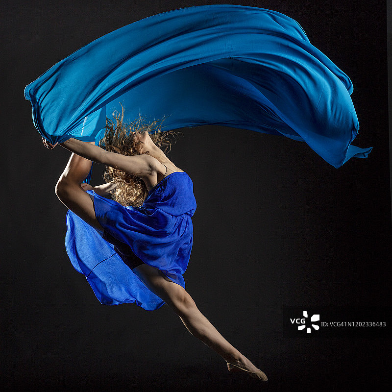 在黑色的背景下，穿着蓝色布料的舞者图片素材