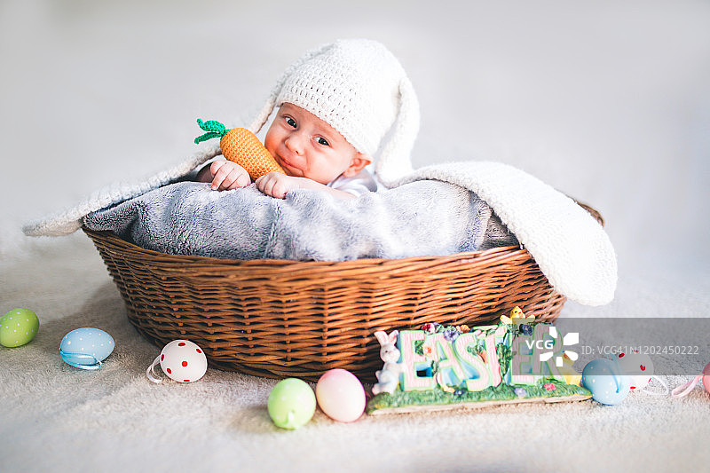 刚出生的小男孩戴着兔耳朵和尾巴，放在篮子里。图片素材