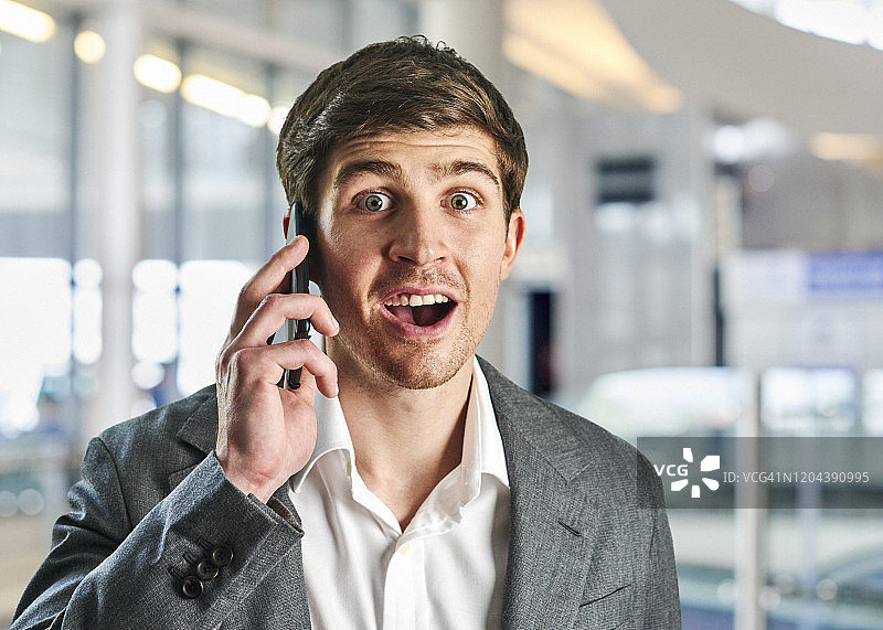 在机场候机楼里，一个年轻的商人用惊讶的表情打电话。图片素材