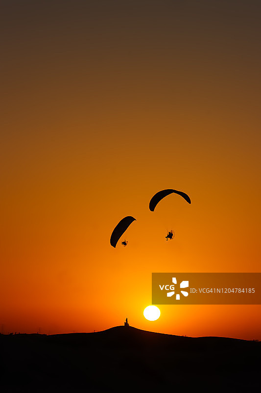 一群人的剪影站在迪拜沙漠日落和滑翔伞飞行上方图片素材