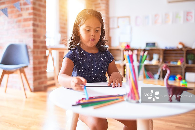 美丽的蹒跚学步的小女孩在幼儿园用彩色铅笔画可爱的画图片素材
