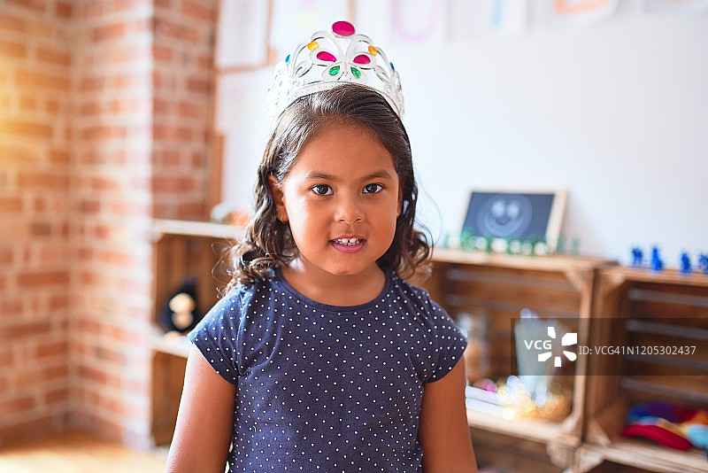 美丽的蹒跚学步的小女孩戴着公主皇冠站在幼儿园里图片素材