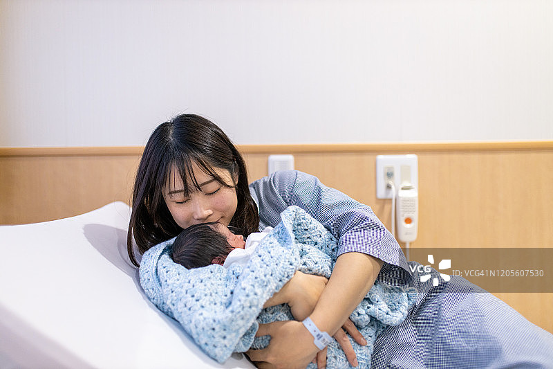 一位年轻的母亲在医院里抱着她刚出生的孩子亲吻图片素材