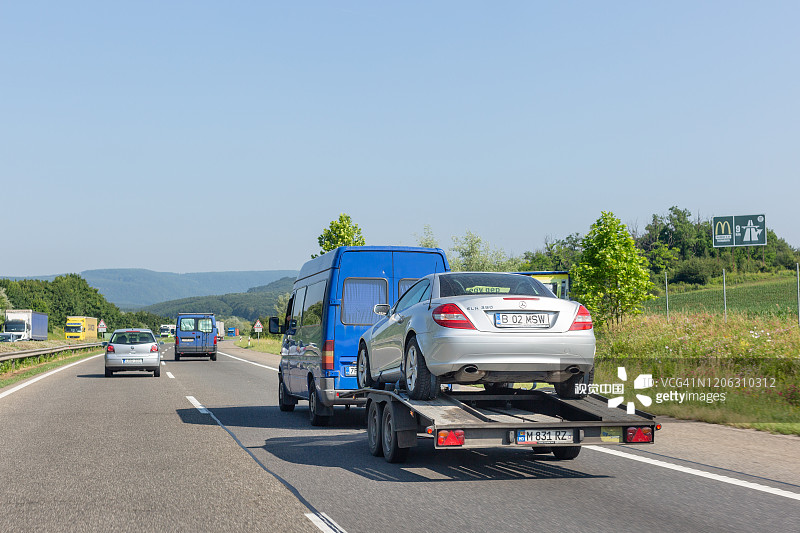 汽车运输车与汽车拖车。蓝色小巴与拖车运输车在公路上运载汽车图片素材