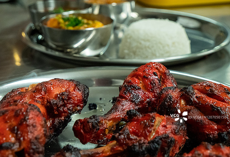 近距离拍摄的一盘熟的印度烤鸡在前景与米饭和其他印度食物在背景。图片素材