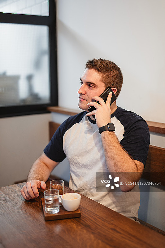 一个年轻人在咖啡店里一边喝咖啡一边用手机图片素材