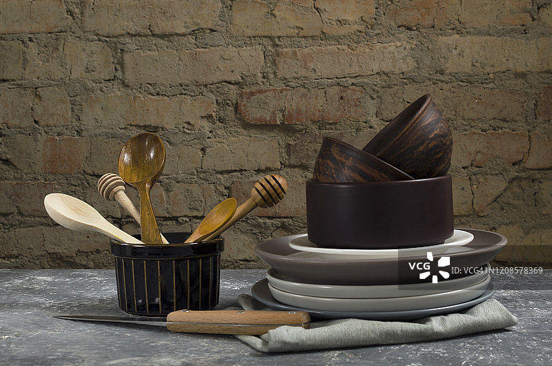 乡村厨房用具的特写，旧砖墙上的桌子上的器具。木制的勺子、粘土和陶瓷盘子、碗和餐巾放在灰色的桌子上。农村大气图片素材