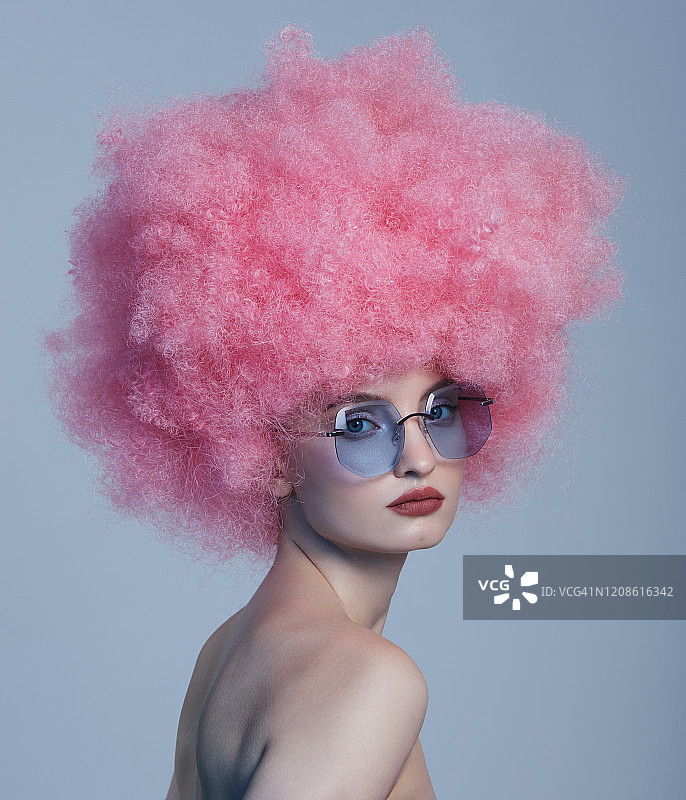 漂亮的年轻女子，一头粉红色的卷发，戴着蓝色的眼镜图片素材