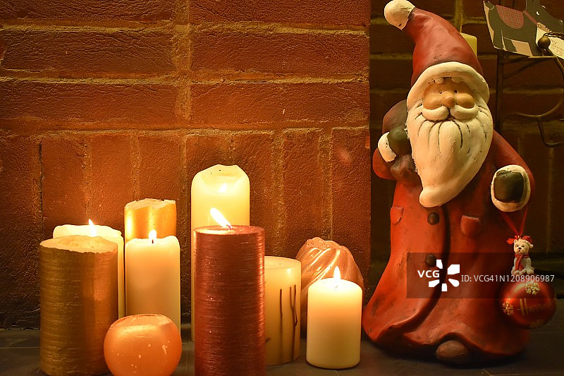 美丽温暖的灯光从靠近墙壁的蜡烛和圣诞老人的娃娃在地板上，家里的装饰，家甜蜜的家图片素材