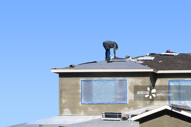 一名熟练的建筑工人正在把沥青瓦铺在新房子的屋顶上。图片素材