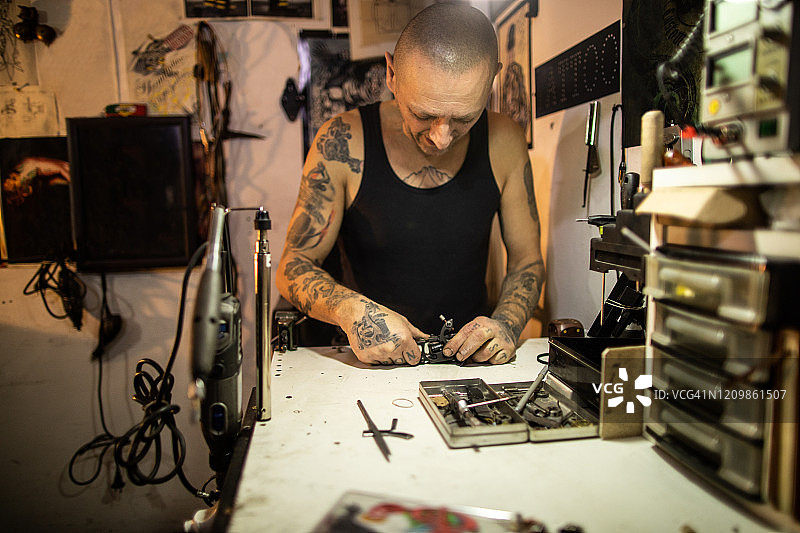 纹身艺术家站在他的工作台前，试图修复他的坏纹身机图片素材