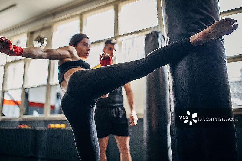 拳击教练看着女拳击运动员在拳击课上踢沙袋图片素材