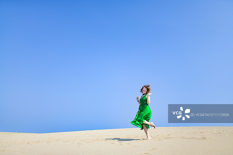穿着绿色衣服的白人女人站在沙丘上。图片素材