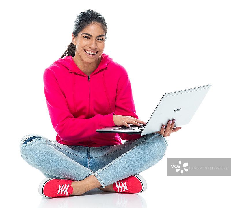 z一代女性穿着帆布鞋坐在白色背景前使用笔记本电脑图片素材