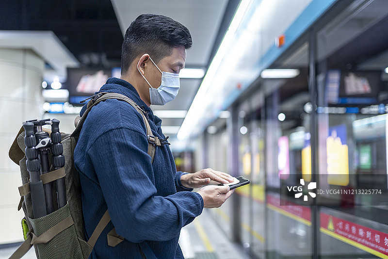 一名亚洲男子在等地铁时擦拭手机屏幕图片素材