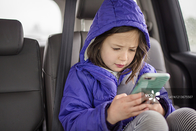 一个小女孩在一次汽车旅行中在汽车后座玩手机图片素材