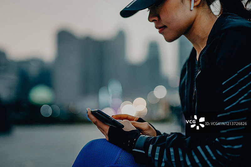 自信、精力充沛的年轻亚洲女运动员，在日落时分，在城市公园里，通过智能手机上的健身应用监控自己的健身进度图片素材