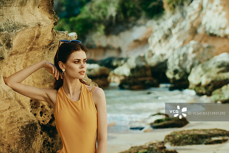时尚照片上的一个年轻女子倚靠在岩石上的海滩上的岩石。图片素材