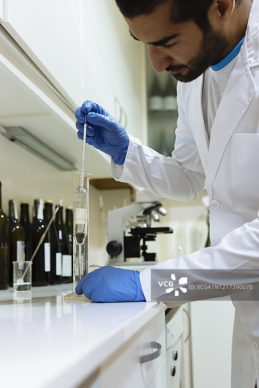 阿拉伯酿酒师穿着白色长袍和手套在葡萄酒实验室工作。图片素材