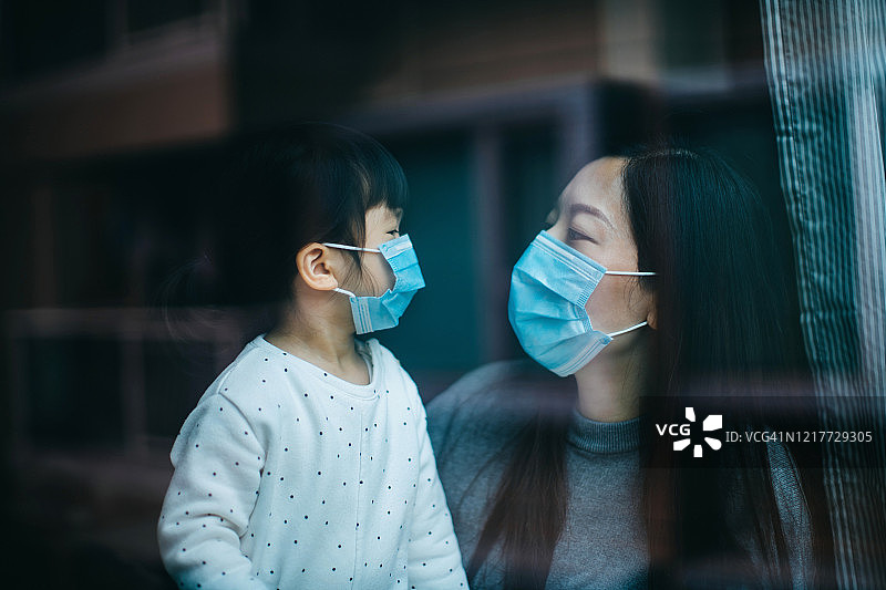 新冠肺炎疫情爆发，年轻的母亲和小女儿戴着防护口罩，在家中自我隔离，以保护和防止病毒传播图片素材
