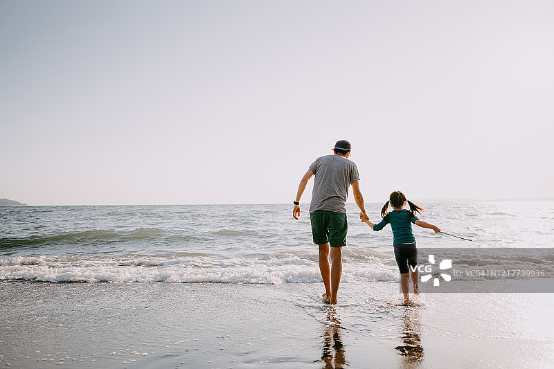 父亲和孩子在海滩上散步的后视图图片素材