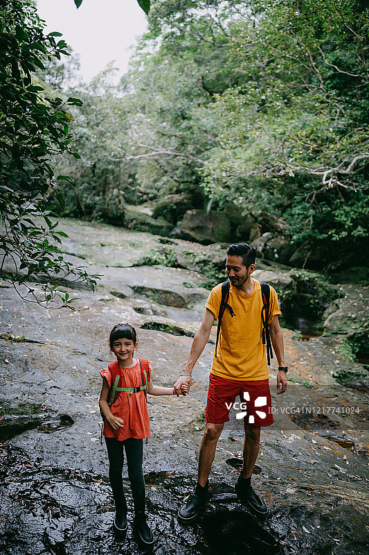 父亲和年幼的女儿徒步穿过森林的河流，冲绳，日本图片素材
