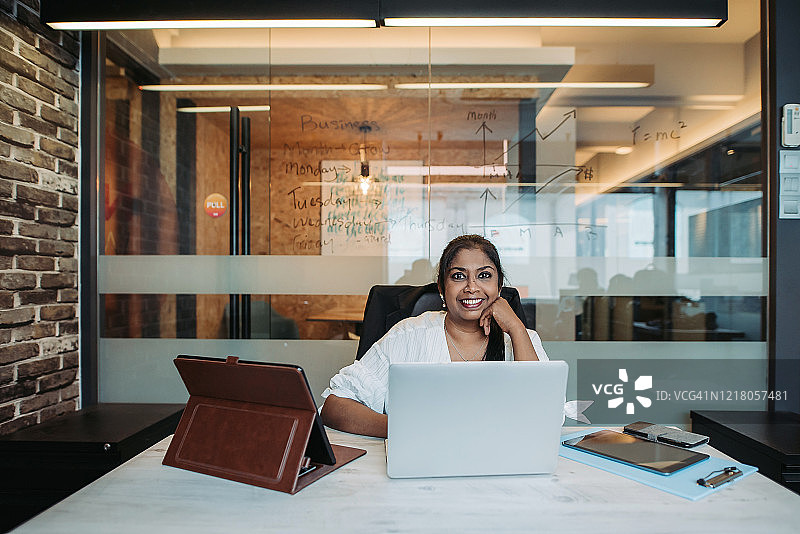 亚洲印度女性经理微笑着使用笔记本电脑和数字平板电脑在她的办公室讨论会议图片素材