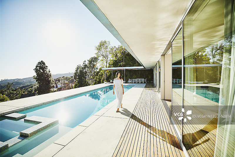 女人走在现代家庭后院的游泳池甲板上图片素材