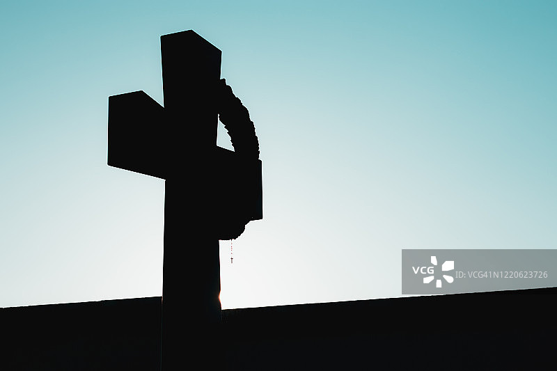黑色的基督十字架轮廓，上面挂着一个小十字架。黑色的欠曝光交叉和明亮的蓝绿色的早晨天空的对比图片素材