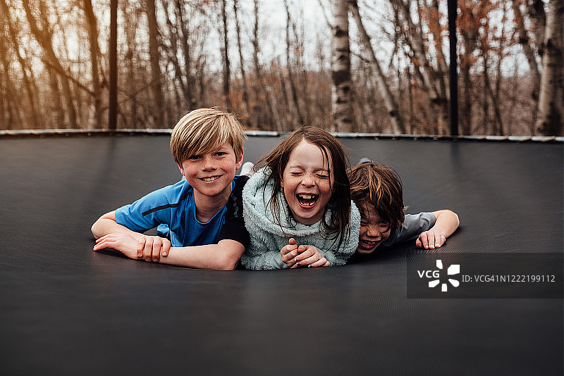 三个微笑的孩子躺在花园里的蹦床上，美国图片素材