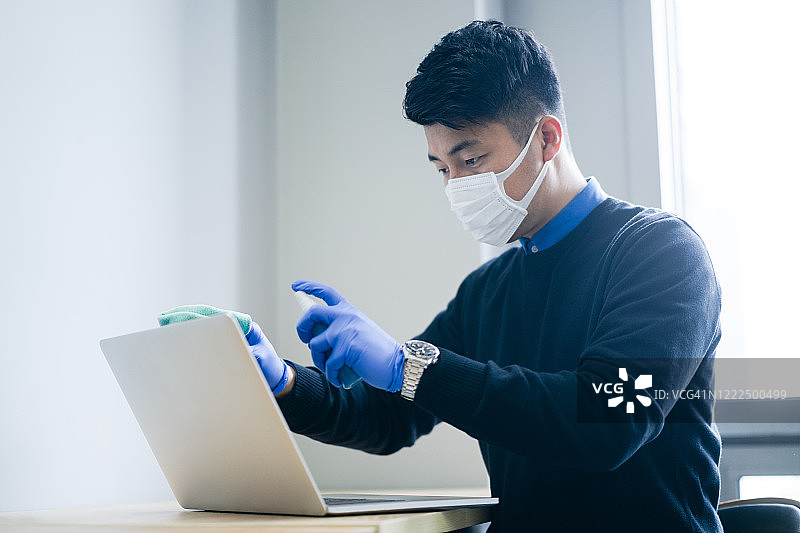 亚洲男子正在用消毒液擦拭笔记本电脑图片素材