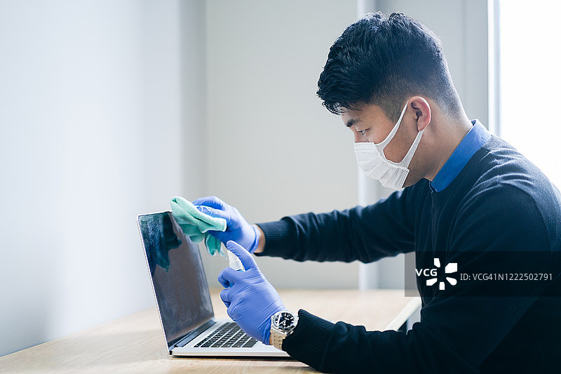 亚洲男子正在用消毒液擦拭笔记本电脑图片素材