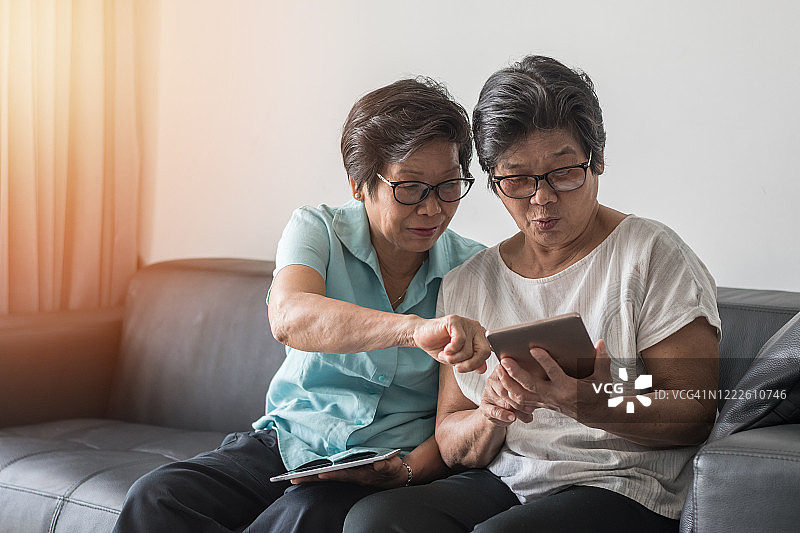 老年社会理念，亚洲老年女性姐妹利用手机数字平板智能手机应用社交媒体网络，通过互联网在朋友圈交流图片素材