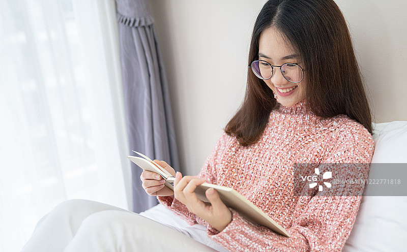 年轻美丽的亚洲女人放松拿着书在卧室与copyspace。微笑快乐亚洲女孩放松知识教育大学亚洲生活方式，回到学校的概念图片素材