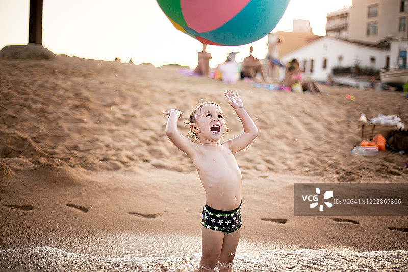 一个男孩举起双手在沙滩上玩球图片素材