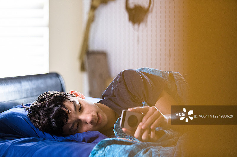在床上，生病的男孩用智能手机玩游戏图片素材