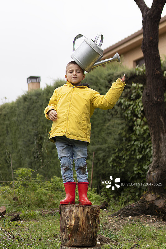 小男孩穿着黄色雨衣，拿着喷壶在花园里干活。图片素材